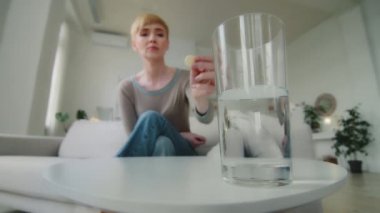 Close-up glass with water standing on table. Young sick ill woman holding dissolving effervescent aspirin pill drop tablet. Relieving headache painful feelings, healthcare medication process concept
