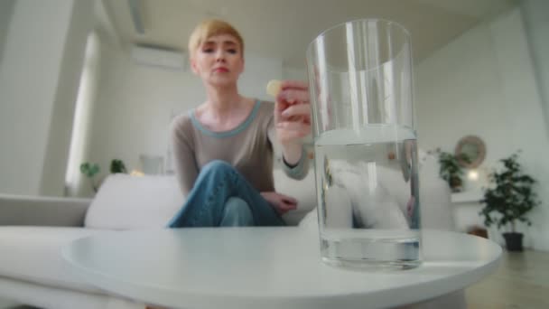 Egy közeli pohár, ahol víz áll az asztalon. Fiatal beteg nő kezében oldódó pezsgőtabletta csepp tabletta. Fájdalomcsillapító fejfájás fájdalmas érzések, egészségügyi gyógyszeres kezelés koncepció — Stock videók