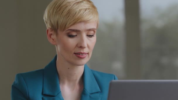 Портрет красивой белой взрослой женщины средних лет 35-40-х годов, деловая женщина, юрист, секретарь бухгалтера с короткими волосами в зеленой куртке, работает на ноутбуке онлайн, глядя в камеру, улыбаясь дружелюбно — стоковое видео