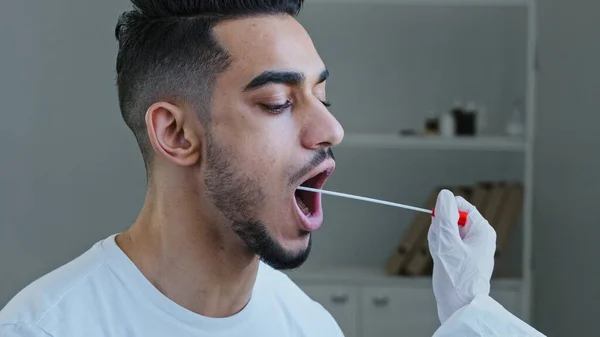 Крупним планом іспанський чоловік арабський пацієнт відкриває рот, пожертвував зразком слини для вірусу інфекції, невідомий медсестра медичний працівник робить pcr тест з обладнанням для кованого-19 коронавірусу для етнічного хлопця — стокове фото