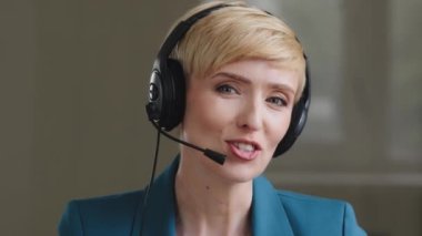 Portrait of beautiful mature middle age 40s business woman with short hair help line manager call center operator advisor wears headset microphone speaks advises clients remotely looking at camera