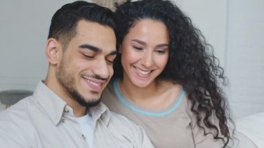 Smiling happy family married couple spaniard spouses boyfriend and girlfriend handsome hispanic man and curly woman cuddling sitting together indoors smile toothy dental read book letter message news