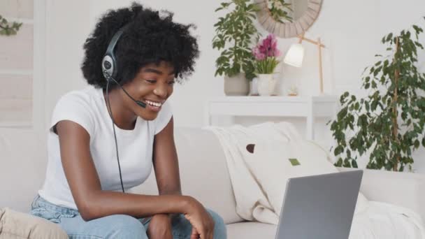 Afrikaanse aantrekkelijke freelancer vrouw dragen headset zitten thuis kijken computer scherm interactie praten met behulp van mic communiceert met een klant of help vriend via internet, werk afstand concept — Stockvideo