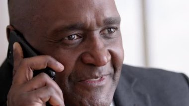 Close-up contented black wrinkled male face makes call answering. Portrait african 50s business man boss leader talking on mobile phone uses smartphone ordering chatting with colleague client smiling