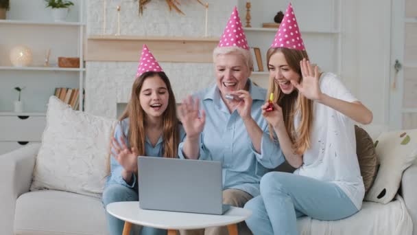 Улыбающаяся молодая взрослая мать, милая очаровательная внучка и взрослая бабушка в смешных шляпах для вечеринок поздравляем родственника день рождения общаться видео звонка чата с помощью веб-камеры приложение — стоковое видео