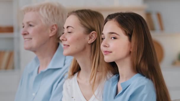 Profiel gezichten in rij drie generatie vrouwen, klein meisje hoofd draaien, glimlachend kijkend naar camera, close-up. Oma uit de 60, volwassen dochter en kleindochter. Familieportretten van meerdere generaties — Stockvideo