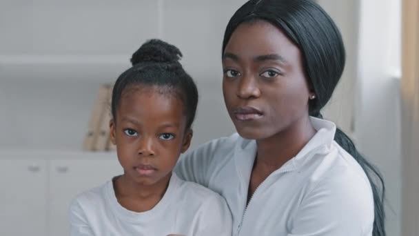 Familie portræt trist afrikansk amerikansk mor omsorgsfuld etnisk kvinde og ked af alvorlig lille afro datter sort førskole barn pige sidder krammer ser på kameraet med bekymrede udtryk indendørs – Stock-video