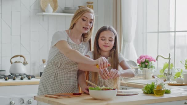 Adult caucasian woman mother and girl child daughter wear aprons stand in home kitchen near table together prepare salad squeeze yellow lemons in plate pouring vegetables ingredients, family cooking — Stockvideo