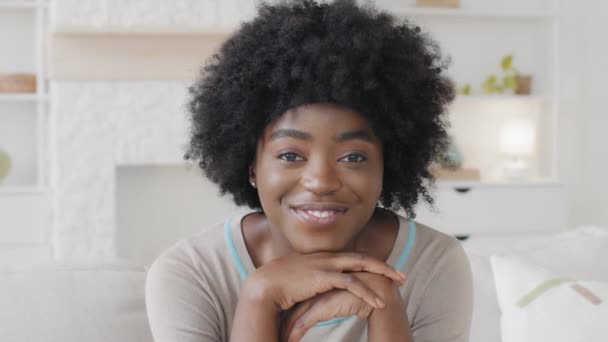 Headshot de jeune africaine métissée positive s'asseoir à l'intérieur dans le salon rêveries regardant la caméra souriant. Femme propriétaire pose à la maison se sent heureux. Locataire, concept de portrait de dame indépendant — Video