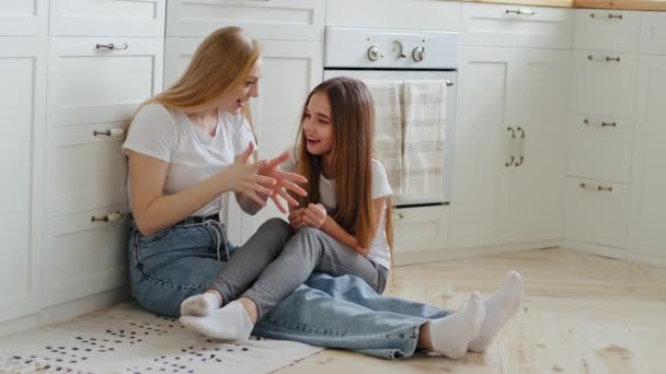 Maturo amorevole madre emotiva con i capelli lunghi si siede sul pavimento della cucina con figlia adolescente e ragazza parlando condividere sogni ed esperienze parlando gesticolando con le mani in aria conversazione casuale al chiuso — Video Stock