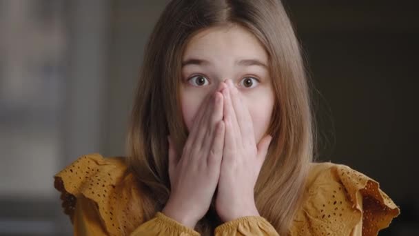 Portrait caucasian girl teenager schoolgirl child daughter younger sister pupil feels shock opens mouth with surprise amaze astonishment wonder covers face with hands looking at camera posing indoor — Stock Video