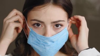 Close-up sad serious female masked face. Portrait caucasian woman young brunette girl patient looking at camera puts on protective medical mask protecting health from coronavirus infection allergy