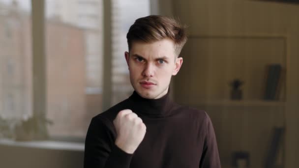 Portrait millennial caucasian guy student male manager leader angry man showing danger gesture with hand shaking fist threatening warns of rage aggression violence standing indoors looking at camera — Stockvideo