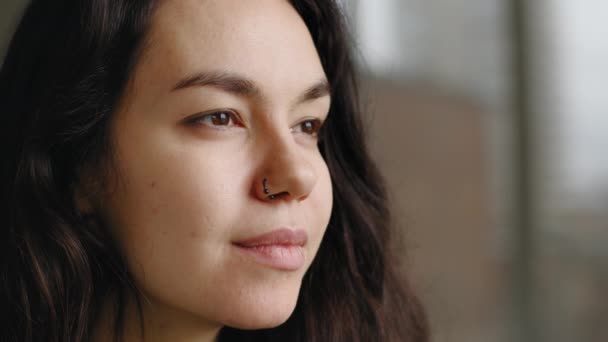 Extreme close-up female young face with perfect skin natural make-up dark eyes pierced nose earring posing looking away. Portrait caucasian millennial woman girl thinking contemplating in window — Stock Video