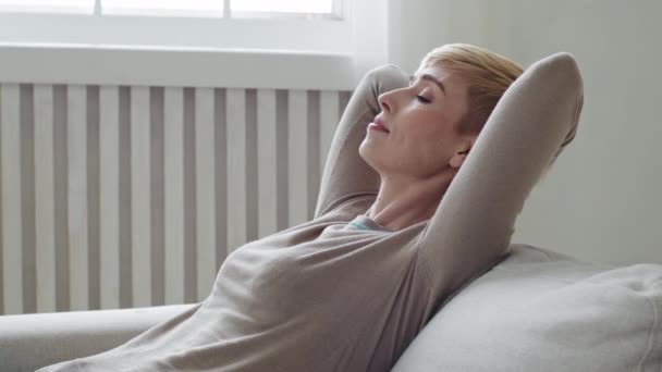 Calme insouciante jeune femme relaxante avec les mains croisées derrière la tête sur un canapé confortable et confortable. Sérieux fatigué salon attrayant dame sur canapé profiter de temps libre week-end de loisirs, rêver seul à la maison — Video