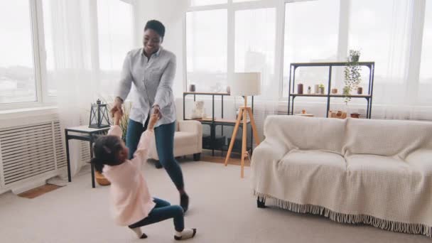 Jovem pai solteiro carinho afro-americano mãe mamãe babá segurando as mãos de etnia negra criança menina filha ativa círculos criança girando pulando jogar jogo se divertindo em casa sala de estar — Vídeo de Stock