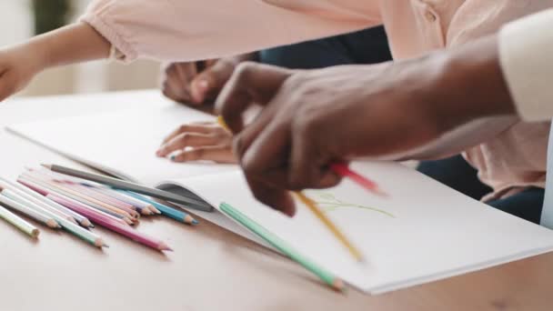 Cropped shot close-up three pairs of hands with dark skin afro american unrecognizable family draw picture on paper hold choose colored pencils parents with daughter girl drawing at home table details — Stock Video