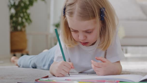 Közelkép kaukázusi kisgyerek lánya óvodás lány koncentrált csecsemő szőke rajzol képet színes ceruzák papíron fekvő padló élvezi rajz hobbi tanulmány otthon, fantasy kreatív koncepció — Stock videók