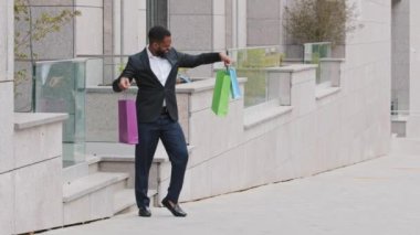 Millennial genç siyah erkek öğrenci, alışveriş merkezinin butik dükkanından kağıt torbalarla çıkan kişisel asistanı. Patron çalışanlar için hediyeler aldı, yeni gardırop, iyi şeyler, mutlu başarılı alışverişler.