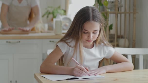 Tiener meisje kind schoolmeisje leerling zitten thuis aan tafel in de keuken doen huiswerk schrijven oefening wiskunde studie leren indoor thuisonderwijs, volwassen moeder kookt deeg met behulp van roller — Stockvideo