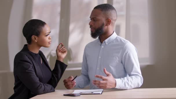 Dois colegas de negócios se comunicam discutindo papel de documento no escritório sentado à mesa, chefe africano líder vendedor masculino agente consulta negra étnica afro mulher comprador empregado falando no local de trabalho — Vídeo de Stock