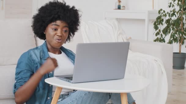 Jovem vencedora afro-americana empolgada olha para o laptop celebra o sucesso online. Senhora de raça mista recebe nova oportunidade de trabalho à distância, lê boas notícias no e-mail, se alegra vitória, se sente motivado — Vídeo de Stock