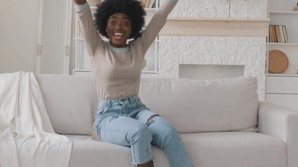 Glücklich entspannt afroamerikanische junge erwachsene schwarze Frau ruhen allein auf bequemen Sofa zu Hause halten Fernbedienung beobachten Sportkanal TV-Programm fühlen sich aufgeregt zu gewinnen. Fankonzept für Fußballspiele — Stockvideo