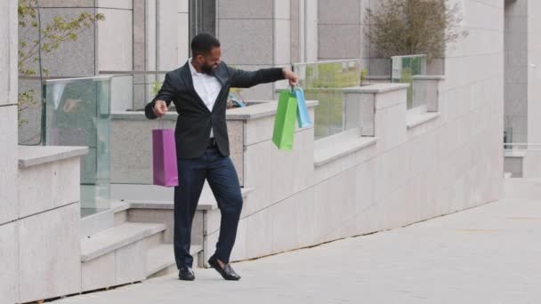 Millennial junge erwachsene schwarze männliche Studentin, persönliche Assistentin, die mit Papiertüten aus einem Einkaufszentrum kommt. Chef kaufte Geschenke für Mitarbeiter, neue Garderobe, gute Dinge, glückliche erfolgreiche Einkäufe — Stockvideo