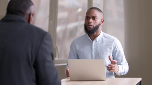 Homem de negócios africano bonito bem sucedido com conversa de laptop irritado com parceiro irreconhecível sentado à mesa do escritório, discutindo sobre questões de negócios compartilhando visões e opiniões projeto de planejamento — Vídeo de Stock