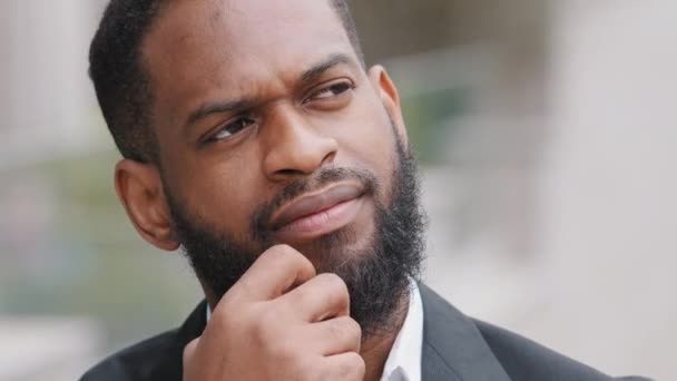 Ciddi sakallı, Afro-Amerikan iş adamı takım elbiseli dışarıda duruyor ve iş için meydan okumayı düşünüyor. Düşünceli erkek yönetici, riskleri göz önünde bulundurarak ekonomik krizden endişe duyuyor. — Stok video