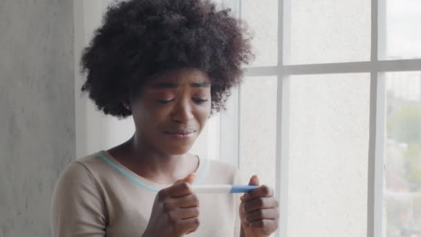 Hamile Afrikalı hamile bir kız pozitif hamilelik testi çubuğu tutuyor ve pişman. Ümitsiz, çatık kaşlı, melez kadın tüp bebek ve kısırlık konseptinden sonra olumsuz sonuçlar aldı. — Stok video