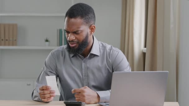 Young African man manages personal budget using calculator calculates expenses spending check bill receipts type in laptop app data digits, planning, worried about loan, bankruptcy, financial troubles — Stockvideo