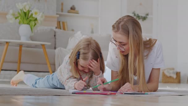 Kaukasiske mor babysitter bærer briller ligger på gulvet i huset med lille datter barn førskole pige studie sammen nyde hobbyer tegning billede tegne med blyanter kunstværk kreativ fantasi – Stock-video