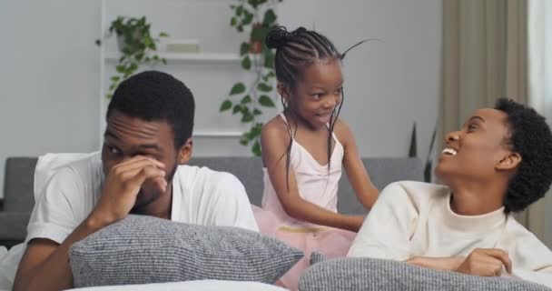 Αφρο-αμερικανική οικογένεια λίγο αστεία κόρη παιδί κορίτσι γαργαλάει παίζει με τη μαμά ξαπλωμένη στον καναπέ διασκεδάζοντας στο σπίτι μαύρο αφρικανός πατέρας που πάσχουν από αλλεργίες πόνο στα μάτια κακή όραση τρίβει το μάτι — Αρχείο Βίντεο
