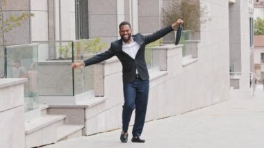 Mutlu Afrika kökenli genç Amerikalı iş adamı dışarıda tek başına dans ediyor, cuma gününü kutluyor, profesyonel başarı, ödül ya da terfi, heyecanlı erkek çalışan zafer dansı konseptinin tadını çıkarıyor.