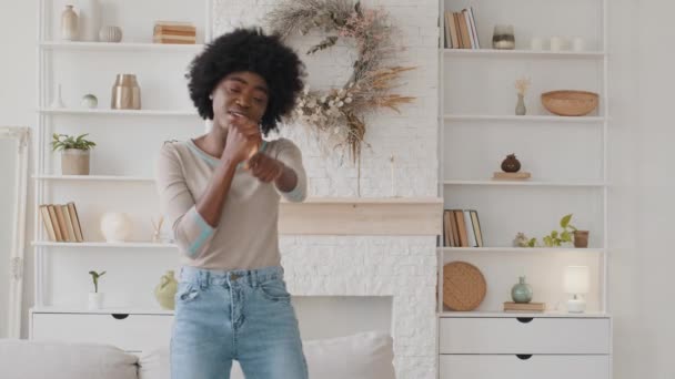 Смішна афроамериканська жінка, яка співає улюблену сучасну ритмічну пісню в перукарню, як мікрофон, танцює, слухає музику, грайлива дівчинка насолоджується притвором співачки вранці — стокове відео