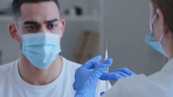 Blick von hinten Ärztin Krankenschwester hält Spritze mit Medikament Impfstoff für covid männliche Patientin hispanische arabische Mann in Maske winkt Hände Nein lehnt Impfungen Proteste gegen Behandlung ab — Stockvideo