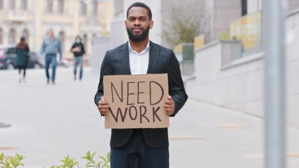 Portrét mladého dospělého černocha stojícího venku s plakátem Need Work. Zbankrotovaný tisíciletý muž s bílým límečkem hledající práci. Smíšené závod podnikatel ukazující kartónové cedule čeká pomoc — Stock video