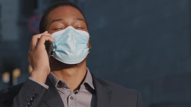 Joven adulto mixto carrera profesional, usando médico mascarilla hombre de negocios haciendo llamada de negocios hablando por teléfono al aire libre, feliz afro americano vendedor disfrutando de la conversación móvil vista de cerca — Vídeo de stock