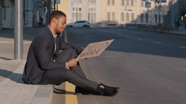 Zoufalý nespokojený afroameričan tisíciletý student v obleku sedící venku na schodech a držící plakát potřebuje práci, černý podnikatel nervózně háže reklamu, zanechává beznadějné zaměstnání — Stock video