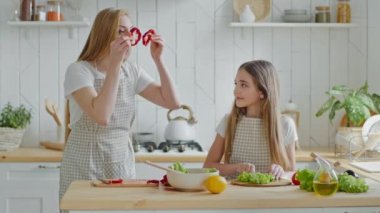 Komik, neşeli, olgun bir anne, genç bir kızla yemek pişiriyor, marul salatası kesiyor, salata hazırlıyor, anne kırmızı biberden parçalar alıyor, gözlüğe bakıp gülüyormuş gibi yapıyor.