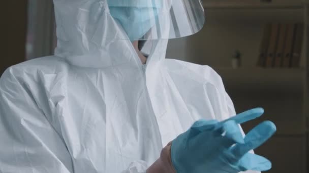 Unrecognizable woman doctor medical worker wears special protective suit uniform puts on rubber latex blue gloves preparing to examine sick patient working in hospital clinic during covid-19 pandemic — Stock Video