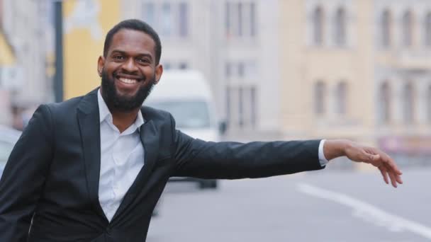 Souriant joyeux jeune homme bienveillant adulte portant des vêtements formels signalant au conducteur de s'arrêter, laisser en voiture, gars joyeux en costume attendant un taxi debout sur le trottoir à l'extérieur. Services de transport urbain — Video