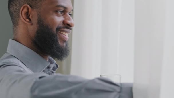 Healthy young African American businessman looking out window drinking pure fresh cold water in office, enjoying healthcare daily habit during workday. Happy employee hydrating thirst at workplace — Stock Video