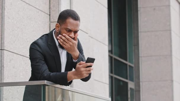 Hombre africano joven frustrado mirando la pantalla del teléfono inteligente, sintiéndose decepcionado con el mensaje de malas noticias recibidas. Estresado de raza mixta millennial hombre de negocios leyendo sms, molesto notificación de préstamo bancario — Vídeo de stock