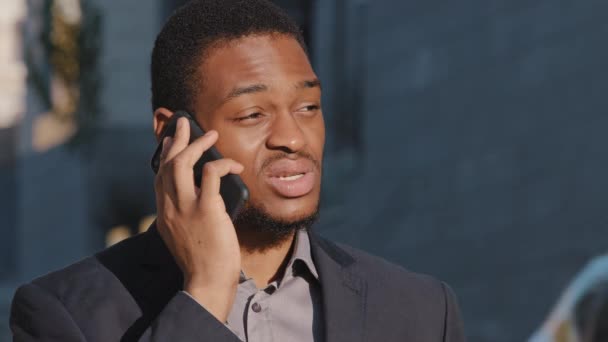 Serious focused millennial African American businessman standing outdoor talking on phone, young mixed race entrepreneur speak on cellphone, solve business issues. Mobile professional communication — Stock Video