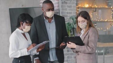 Çok ırklı iş ortakları iki çok ırklı kadın ve Afrikalı olgun patron maske takıyor şirket ofisinde maske takıyor projeyi tartışıyor belgeleri okuyor stratejiyi rapor ediyor