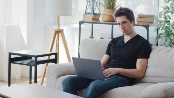 Concentrated adult business man millennial guy student male freelancer client buyer sitting on couch at home with laptop working in computer quarantine online chatting shopping uses wi-fi application — Stock Video