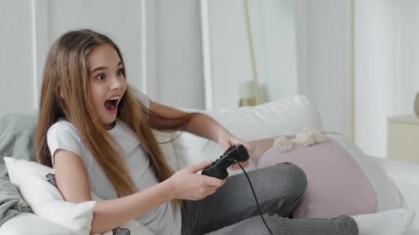 Wesoły biały uczennica nastolatka szczęśliwy active dziewczyna córka grać w gry wideo online sam w domu siedzi na kanapie grać konsola gospodarstwa joystick kontroler emocjonalnie gier wideo — Wideo stockowe