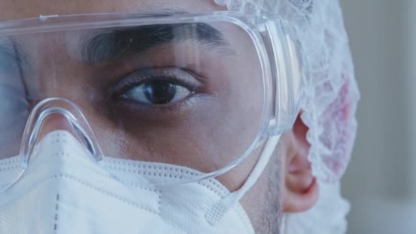 Primer plano hombre negro cansado y somnoliento ojo medio cara hombre médico usando gafas de protección personal médico ropa especial uniforme de trabajo en el hospital mirando coronavirus cámara covid-19 epidemia — Vídeo de stock